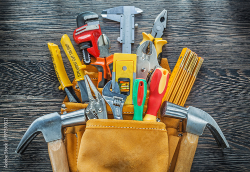 Leather toolbelt building tools on wooden board directly above photo