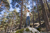 hiker sport woman standing on top of great rock in the forest, hand on her forehead looking at, in Navacerrada mountain, Guadarrama Natural Park, Madrid, Spain 
