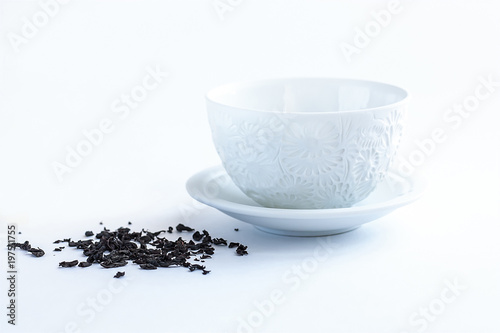 white cup with a floral pattern and a saucer on a white background with scattered tea next to it