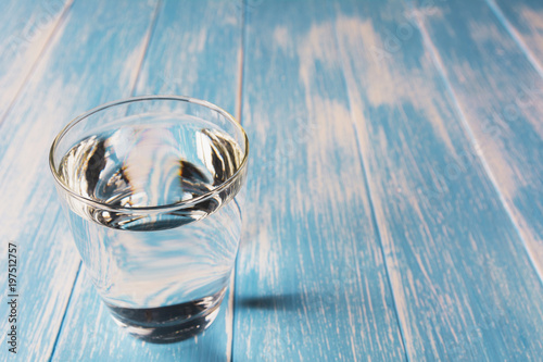 Water in glass on blue and wooden table background.