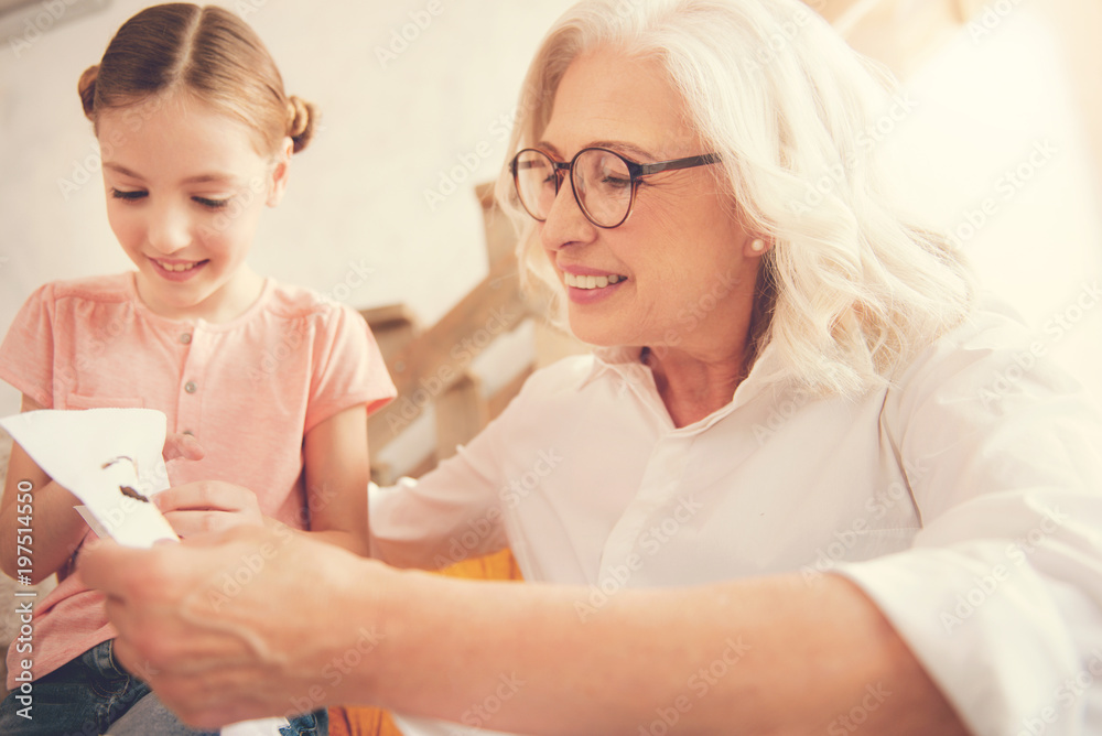 Family time. Happy positive elderly woman smiling and embroidering while spending time with her granddaughter Family time. Happy positive elderly woman smiling and embroidering while spending time with her granddaughter