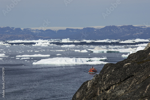 Giant Icebergs of Illulisat, Greenland, floating on water, a popular cruise destination. Small life boat amongst the giant Icebergs