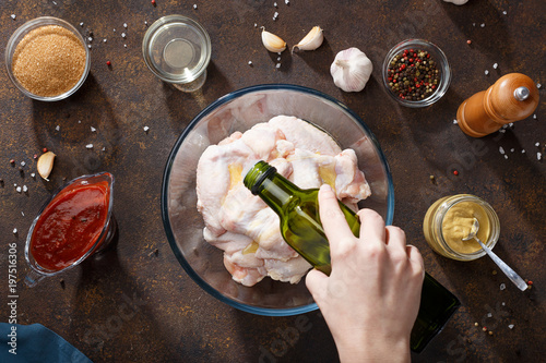 Hand pouring oil over raw chicken wings in glass bowl.
