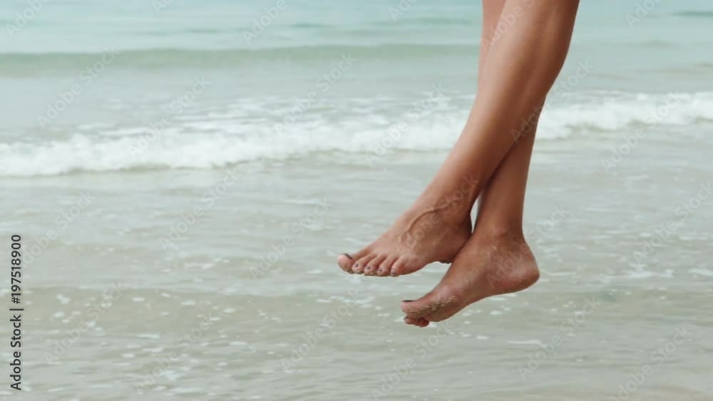 Slow motion closeup of slim female legs swinging at the sea backround. Woman is relaxing on the swing at the beach
