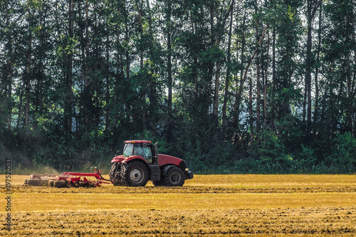 Red farming tractor is working in the field. Disc harrow for crushing stubbles. Agricultural landscape.