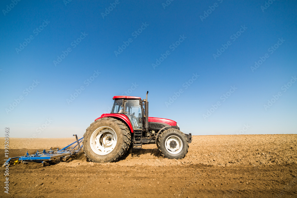 Obraz premium Tractor cultivating field at spring
