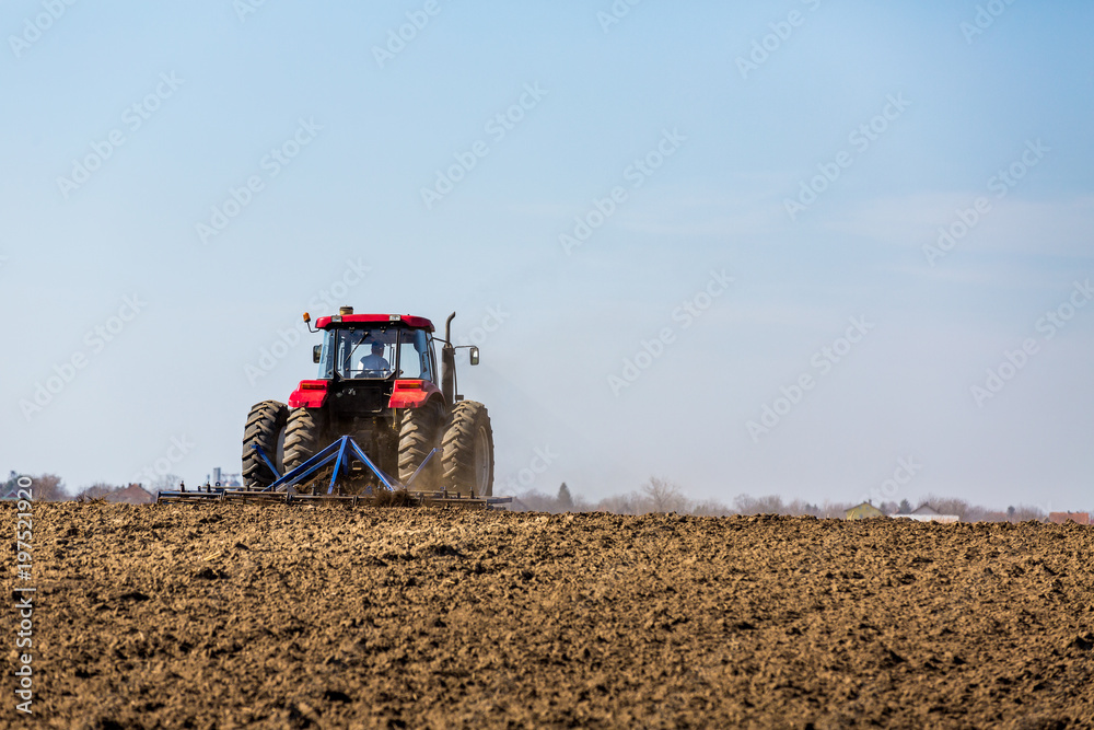Fototapeta premium Tractor cultivating field at spring