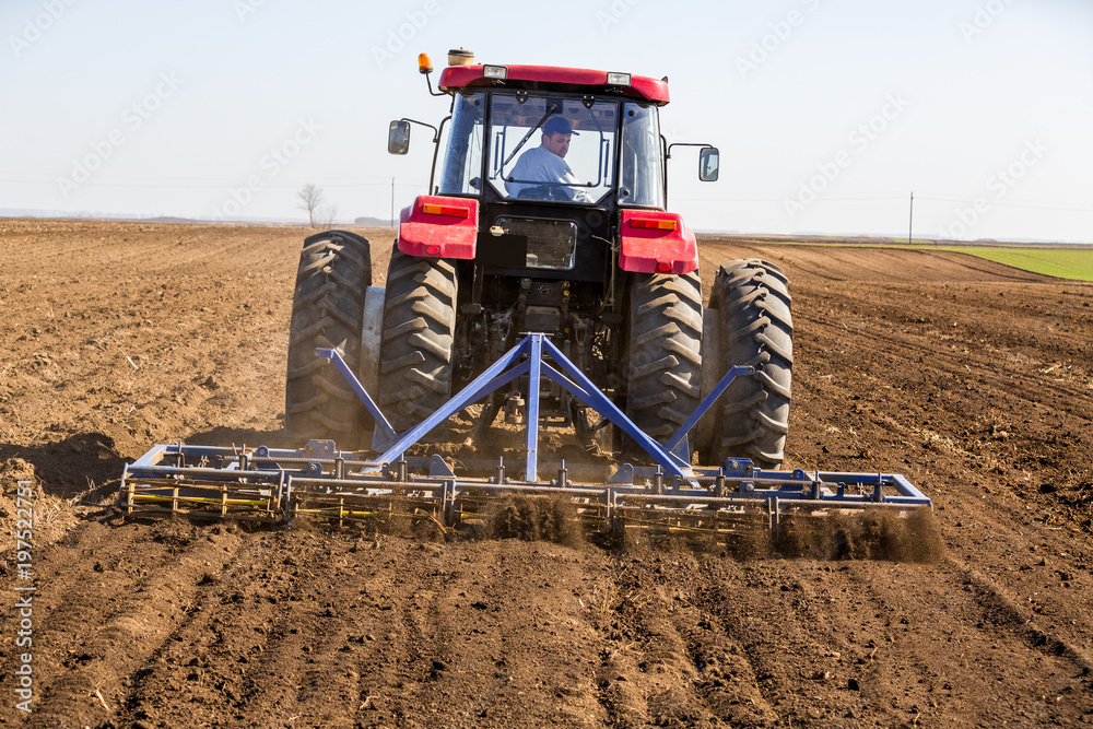 Fototapeta premium Tractor cultivating field at spring