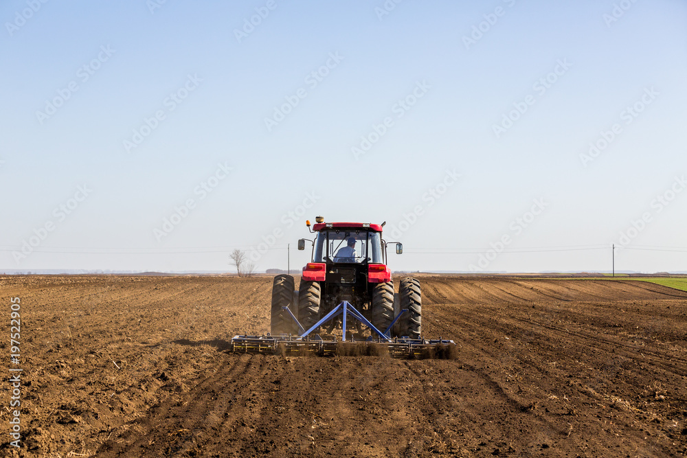 Fototapeta premium Tractor cultivating field at spring