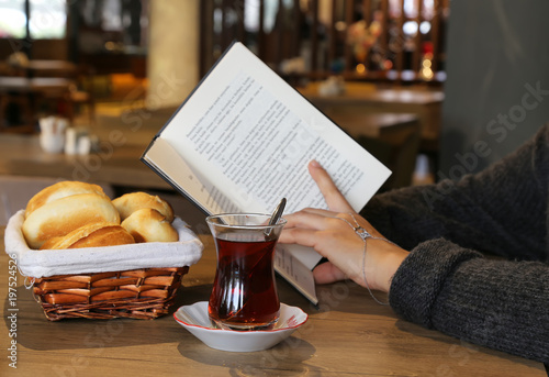 breakfast with tea and bread in a basket . Female read a book .