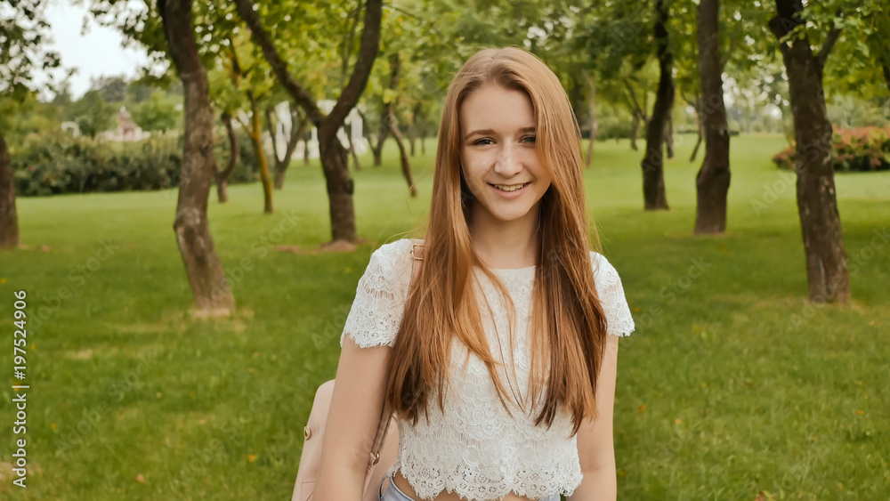 A young girl is engaged in a walk in the park, looking at a smart clock on her arm and receiving a pulse measurement. Health. Sport. Recreation. Summer.