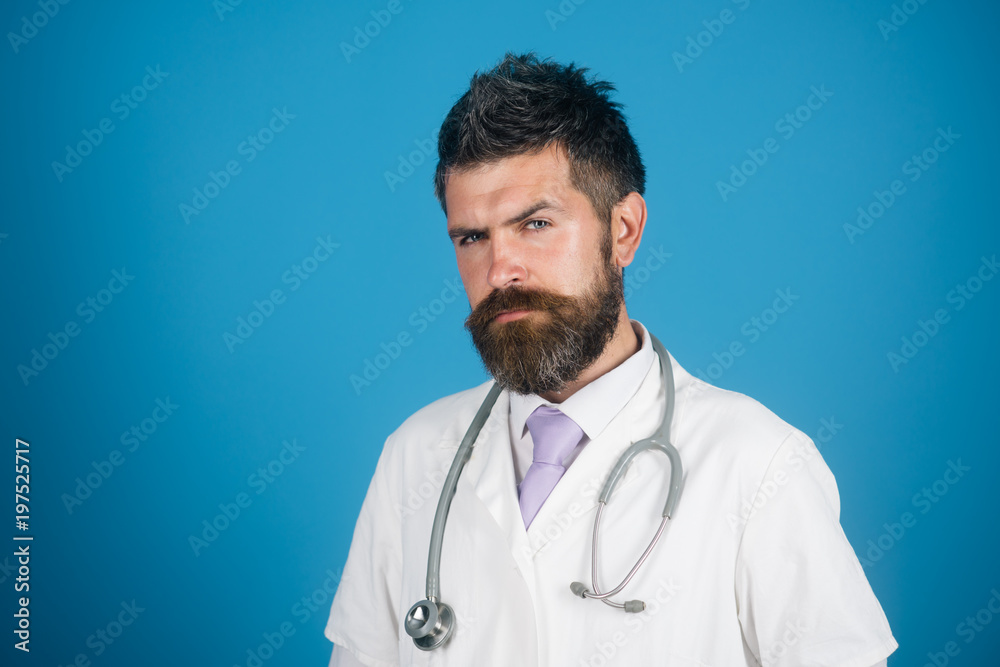 Physician with beard in white medical robe. Medical and healthcare concept - doctor with stethoscope in hospital. Medicine and health - serious handsome male doctor in white medical gown. Copy space. Physician with beard in white medical robe. Medical and healthcare concept - doctor with stethoscope in hospital. Medicine and health - serious handsome male doctor in white medical gown. Copy space.