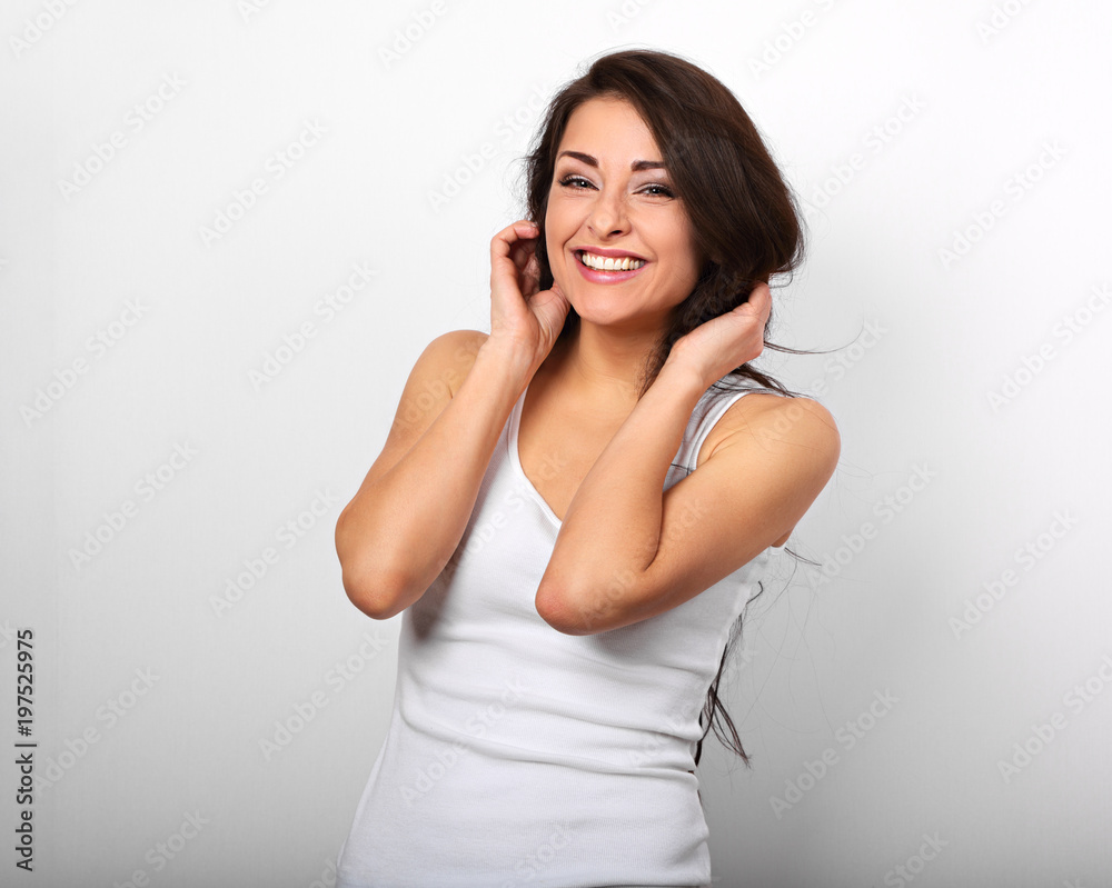 Beautiful positive excited laughing young woman holding the hands the hair in white shirt and with toothy smile on white background Beautiful positive excited laughing young woman holding the hands the hair in white shirt and with toothy smile on white background