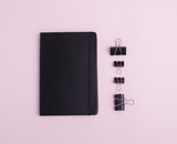 Composition of black stationery such as notebook and paperclips isolated on light pink background. Flat lay. Copy space. Top view