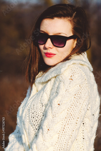 Pretty young stylish woman posing in a trendy fashion coat walks in the park on a sunny winter day