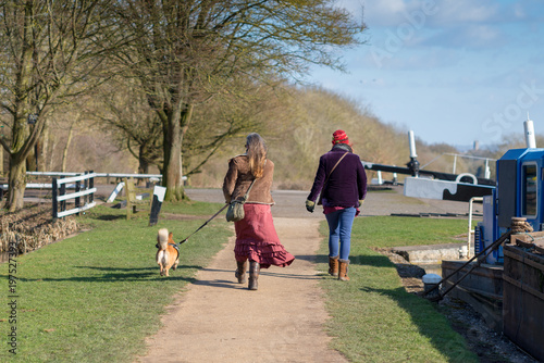 Valokuva Hippy women in bright clothes walking small dog by canal with boats and trees in