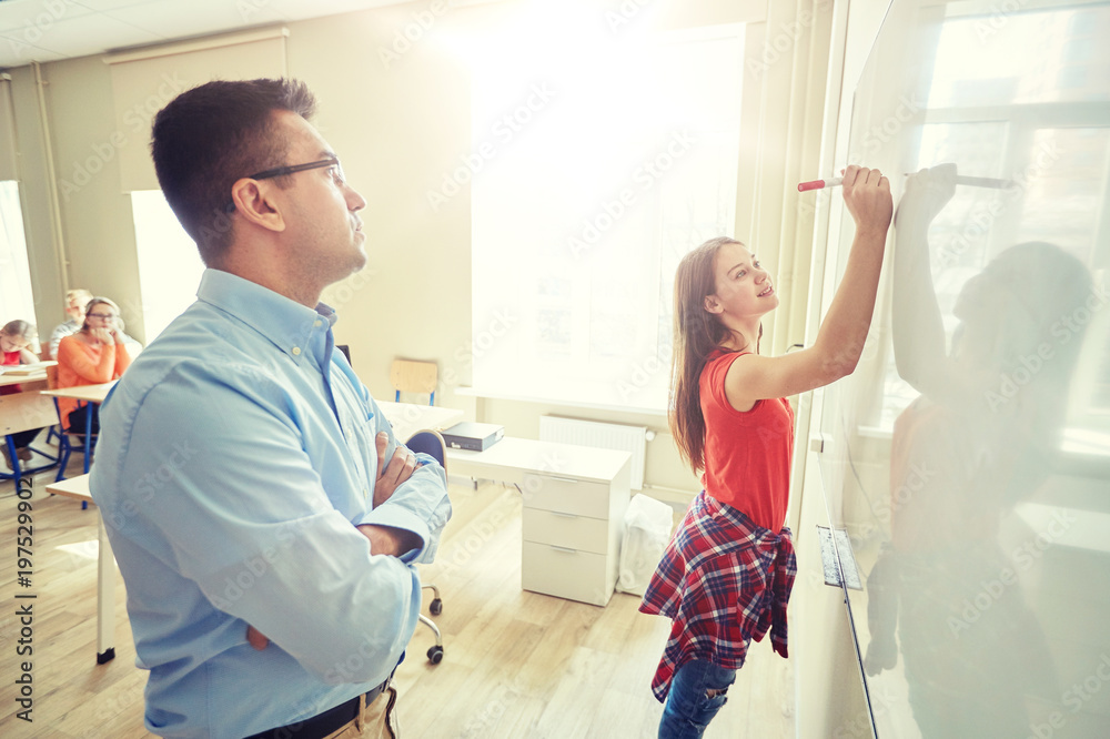 Obraz premium education, school, learning and people concept - student girl writing something on blank white board and teacher in classroom