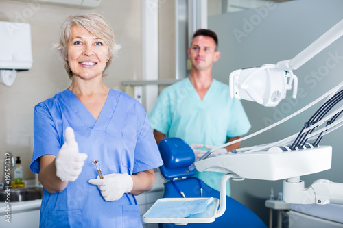 Smiling mature woman dentist in protective gloves showing thumbs up