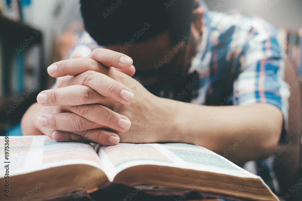 Man praying, hands clasped together on her Bible. - obrazy, fototapety, plakaty 