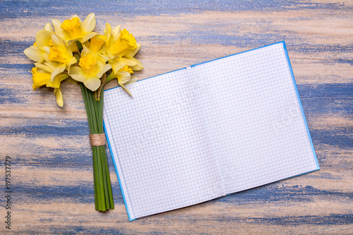 Fototapeta Naklejka Na Ścianę i Meble -  Notepad on a wooden board. Yellow daffodils flowers on a wooden table. Bloomed blue paint. Background with space for text. View from above, flat lay design.