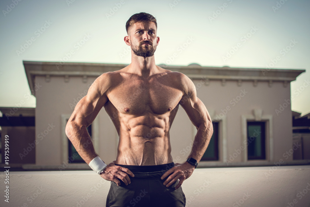Obraz premium Sexy athletic man showing muscular body and six-pack abs outdoors.