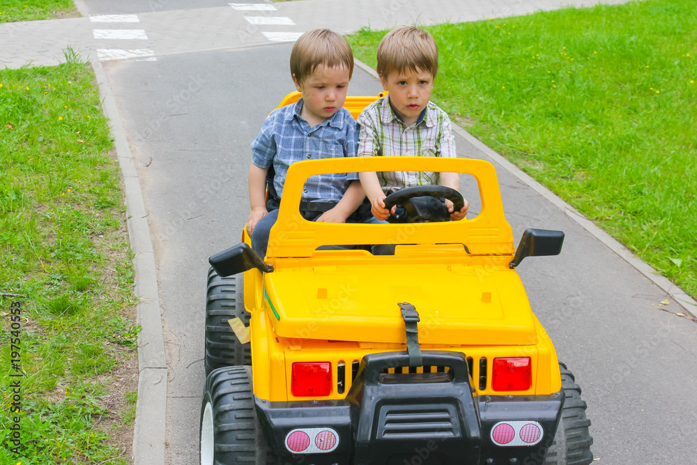 Children in the park ride on an electric car. The boys are riding in an electric car along the paths in the park.