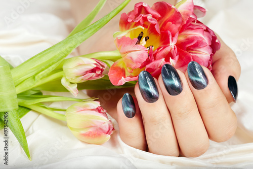 Hand with manicured nails with cat eye design holding pink tulip flower