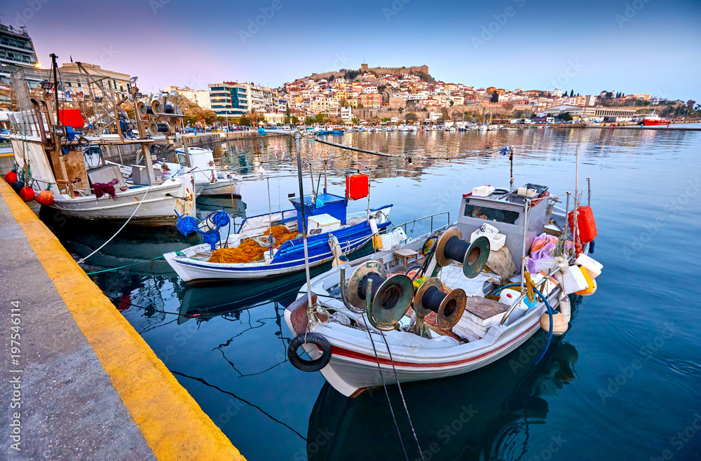 Seaside city of Kavala in Greece. Coloful evening scene, eastern Macedonia, Europe. Greek fishing boats. View on dock for boats and yachts in a beautiful spring evening.