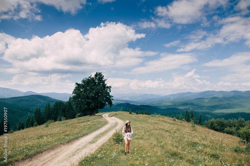Girl in a hat is walking on the road with a stunning mountains view