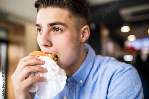 Happy handsome man eating burger in cafe
