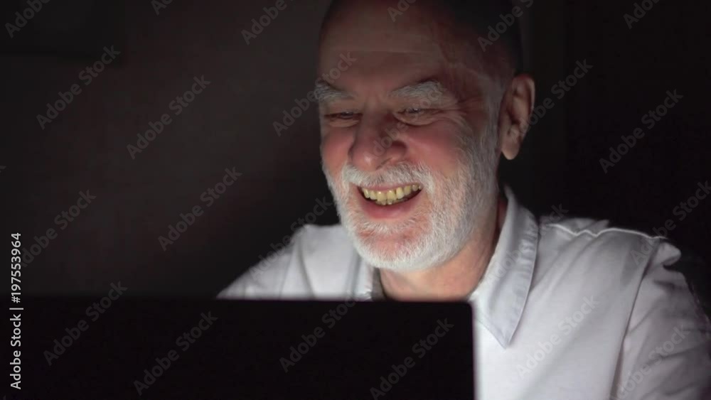 Tired overworked businessman at home working on laptop with documents late at night. Checking data for annual financial report. Secretly using computer hiding from people. Dark only face illuminated Tired overworked businessman at home working on laptop with documents late at night. Checking data for annual financial report. Secretly using computer hiding from people. Dark only face illuminated