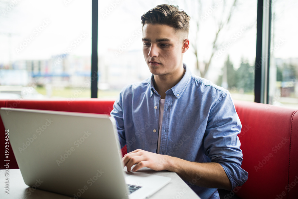Young man freelancer chatting on mobile phone while sitting front open laptop computer in cafe