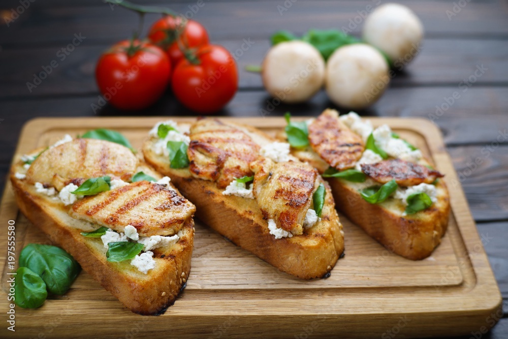 Delicious traditional Italian antipasti bruschetta with grilled chicken, ricotta and basil on wooden board, close up