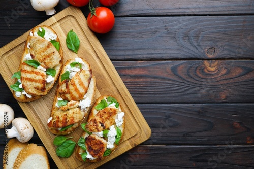 Delicious traditional Italian antipasti bruschetta with grilled chicken, ricotta and basil flat lay on wooden table. Food background for restaurant or menu