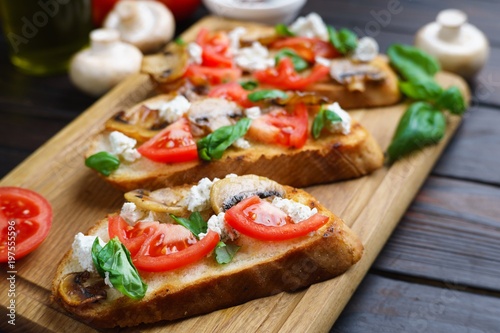 Delicious traditional Italian antipasti bruschetta with chopped tomatoes, ricotta and basil on wooden board, close up