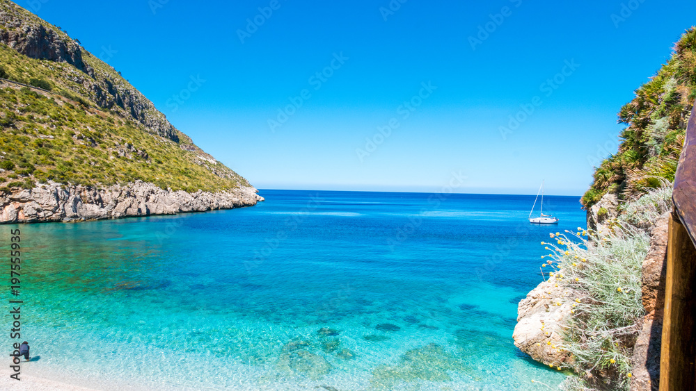 A sailing boat into the turquoise Mediterranean Sea, at San Vito Lo Capo, Sicily, Italy.