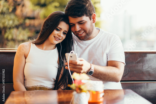Portrait of couple using smartphone and listening to music in cafeteria or restaurant