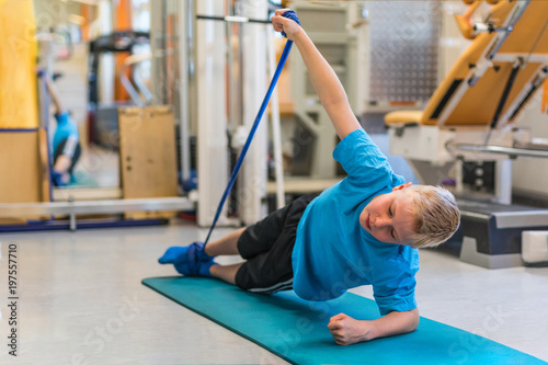 Kind bei der Physiotherapie trainiert mit einem Physiotape auf einer Gymnastikmatte