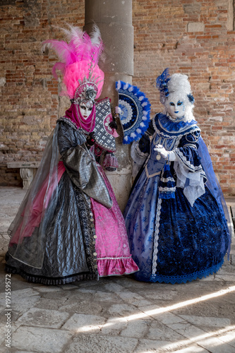 Masked women in ornate blue and pink costumes with fans in an inner courtyard during the Venice Carnival (Carnivale di Venezia)