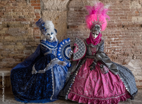 Masked women in ornate blue and pink costumes with fans in an inner courtyard during the Venice Carnival (Carnivale di Venezia) © Lois GoBe