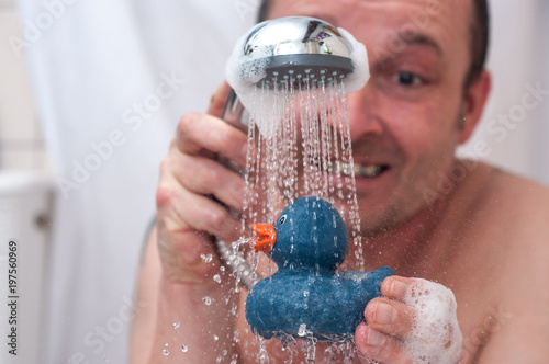 portrait of expressive man playing with rubber duck toy in shower