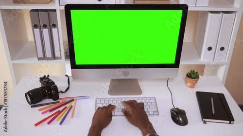 top view on creative workspace. white desk with photo camera green screen on monitor computer. woman hands typing on keyboard