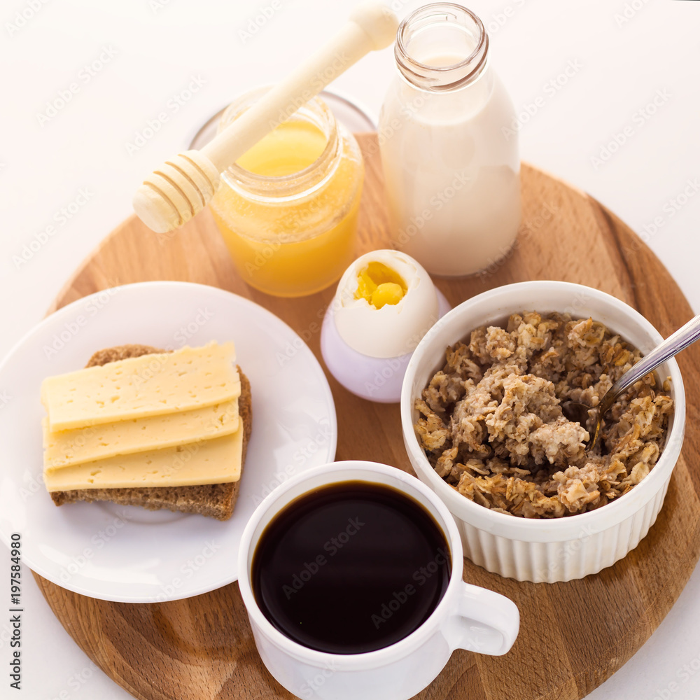 healthy breakfast fresh cereal, cheese sandwich, hard boiled egg, milk bottle, coffee cup and honey jar, toned warm sunny morning light