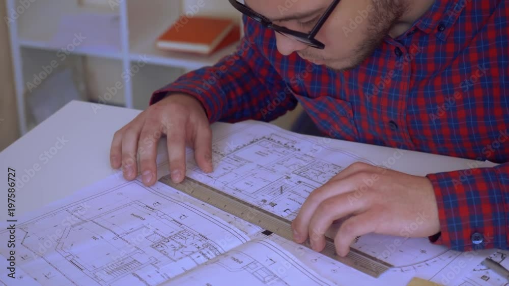 young builder works in the office. professional designer or engineer sitting at the desk with drawing holding a ruler measures objects young builder works in the office. professional designer or engineer sitting at the desk with drawing holding a ruler measures objects