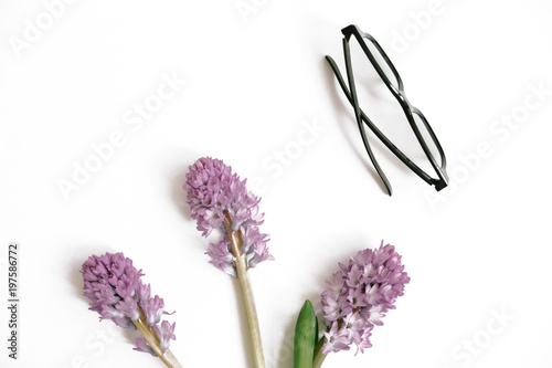 Fototapeta Naklejka Na Ścianę i Meble -  Lilac hyacinth flowers, green leaves and glasses on white background. Flat lay, top view. Summer composition