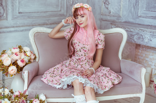 Beautiful young woman doll in a pink dress in a room with flowers, sitting on the couch, lolita. Japanese street fashion.