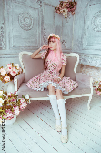 Photography Beautiful young woman doll in a pink dress in a room with flowers, sitting on the couch, lolita
