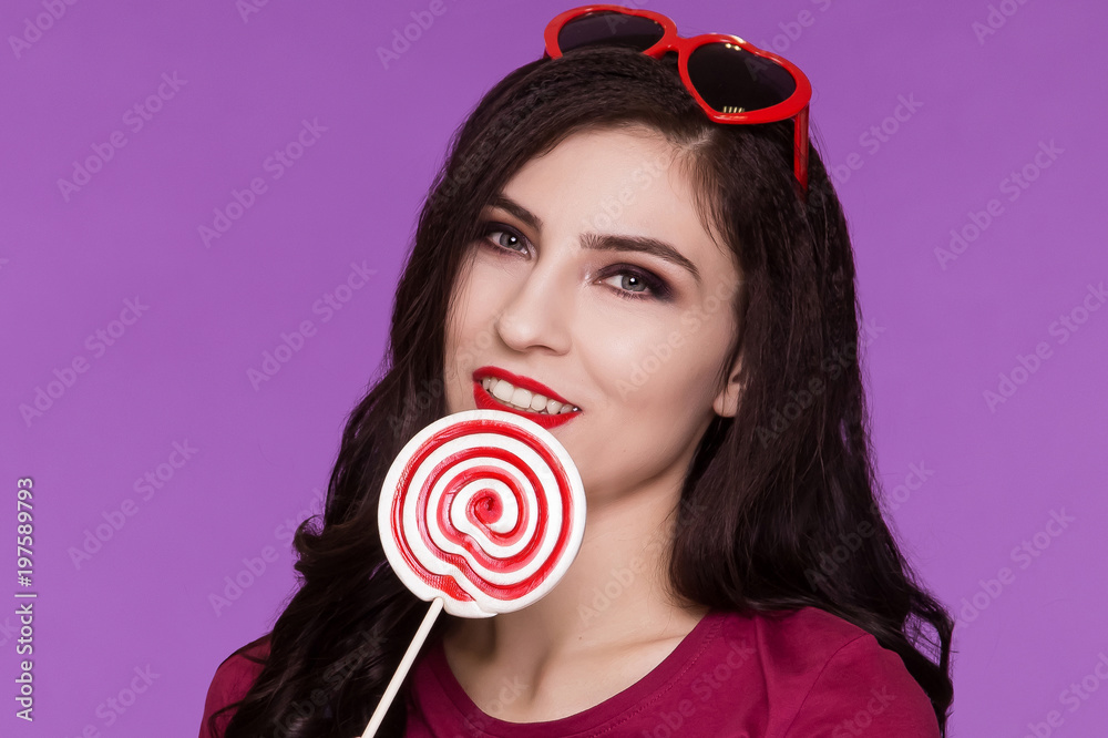 Beautiful brunette woman holding a lollipop and smiling. The heart is wearing sunglasses. Retro image.