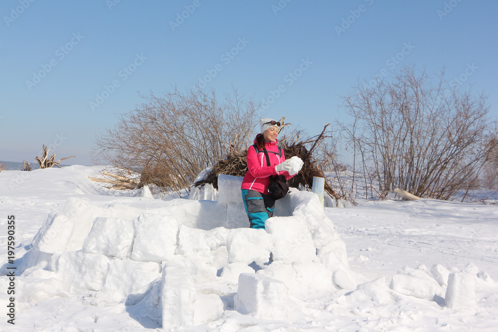 Happy woman a red jacket building an igloo on a snow glade in the winter,  Siberia, Russia