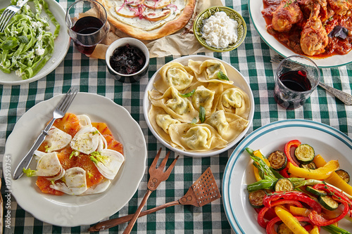 Traditional italian tuscan family dinner with homemade pasta and chicken cacciatore, focaccia and salad served on a table covered with green checkered tablecloth